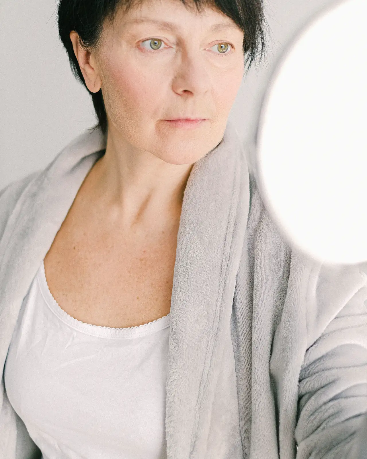 Woman with grey hair in soft light, eyes lowered