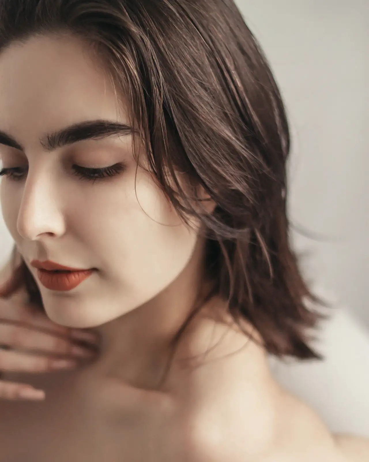 Young woman with brown hair touching her neck, eyes closed