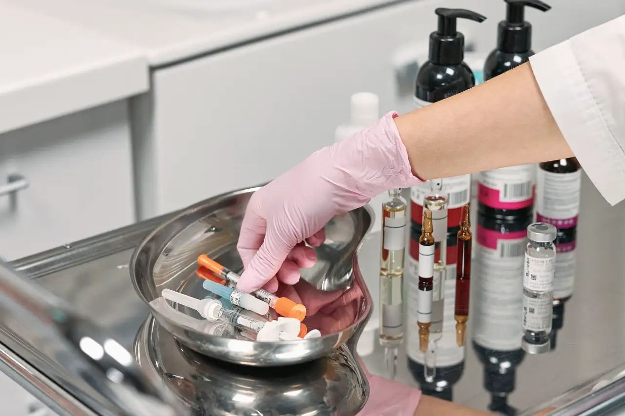 Gloved hand arranging sterile syringes on a stainless tray in a treatment room